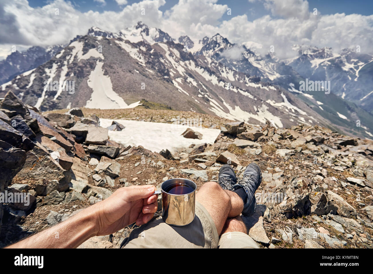 L'uomo coppa di ritegno con il tè caldo con vista delle montagne innevate con sfondo con cielo nuvoloso Foto Stock