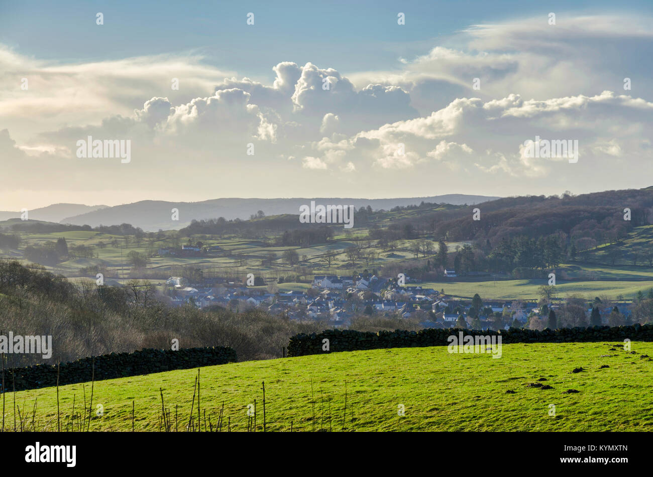 Un campo verde con un villaggio al di là e gowing cumulous clouds ont eh orizzonte Foto Stock