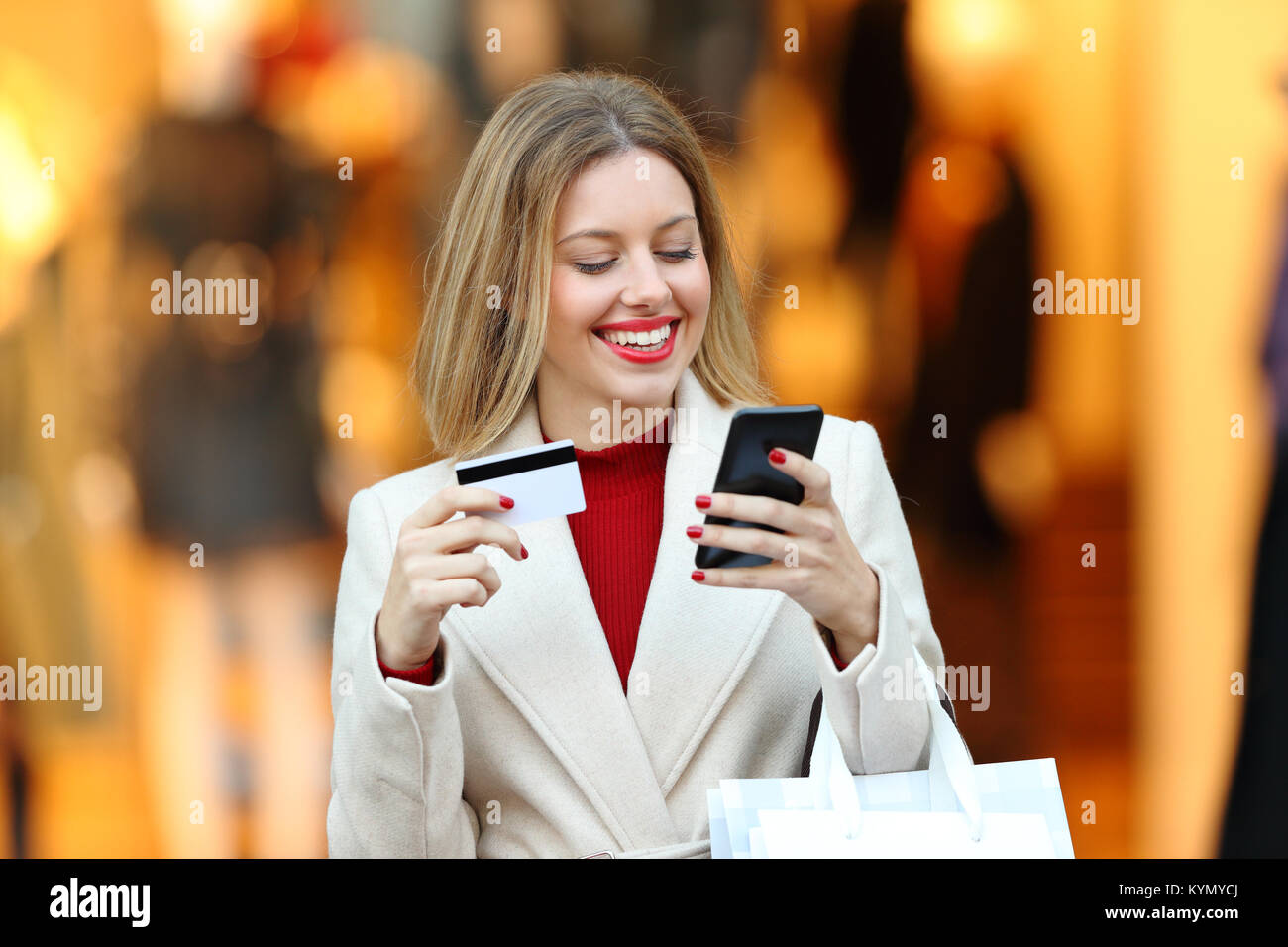 Vista anteriore verticale di un felice shopping shopper pagando con carta di credito online con uno smart phone in un centro commerciale di inverno Foto Stock