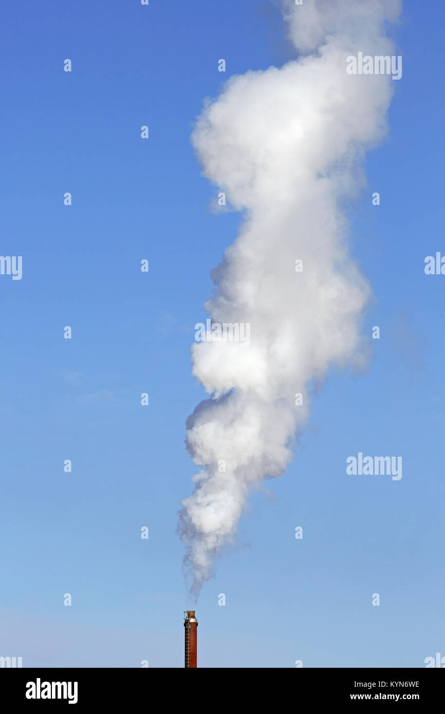 Camino industriale / smoke stack fumaiolo / contro il cielo blu su un giorno windless Foto Stock