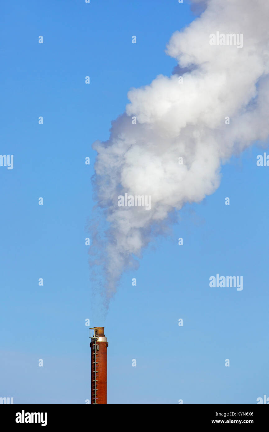 Camino industriale / smoke stack fumaiolo / contro il cielo blu su un giorno windless Foto Stock