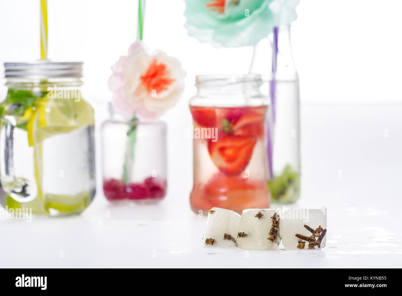 Vasi di acqua con frutti e bacche decorate con fiori di messa a fuoco selettiva su cubetti di ghiaccio in primo piano Foto Stock