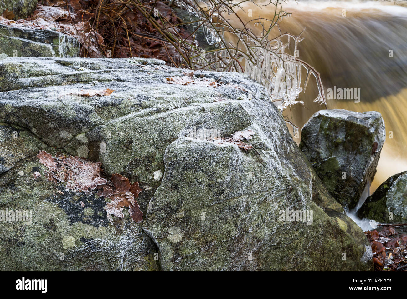 La brina e il ghiaccio sul masso di granito con whitewater rapido in background. Foto Stock