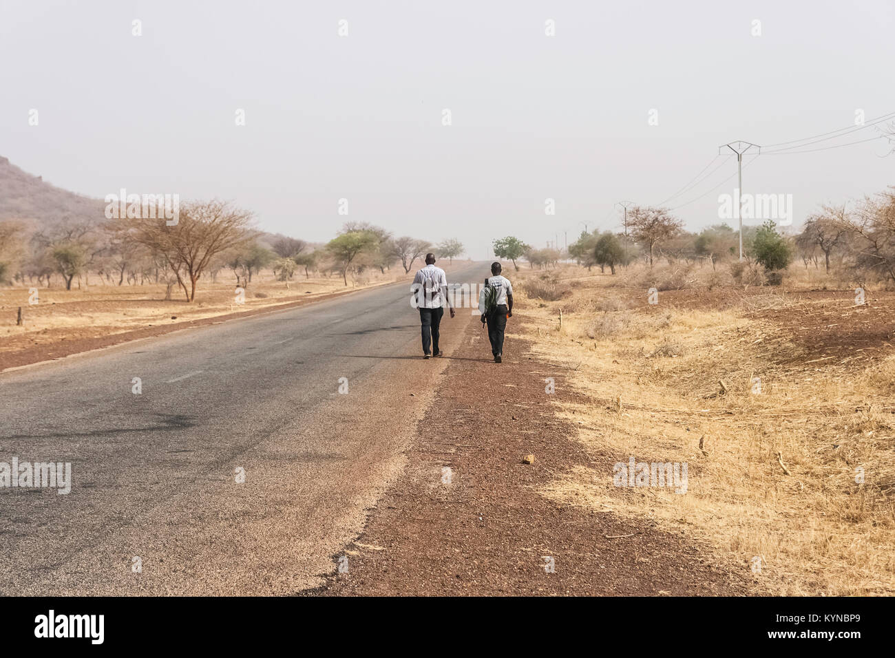Vista posteriore di due uomini africani a piedi lungo una strada di campagna, il Sahel, nel nord del Burkina Faso, Africa occidentale Foto Stock