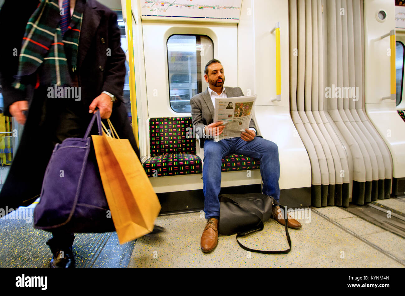 Londra, Inghilterra, Regno Unito. L'uomo leggendo un giornale su un metro di Londra treno tubo Foto Stock
