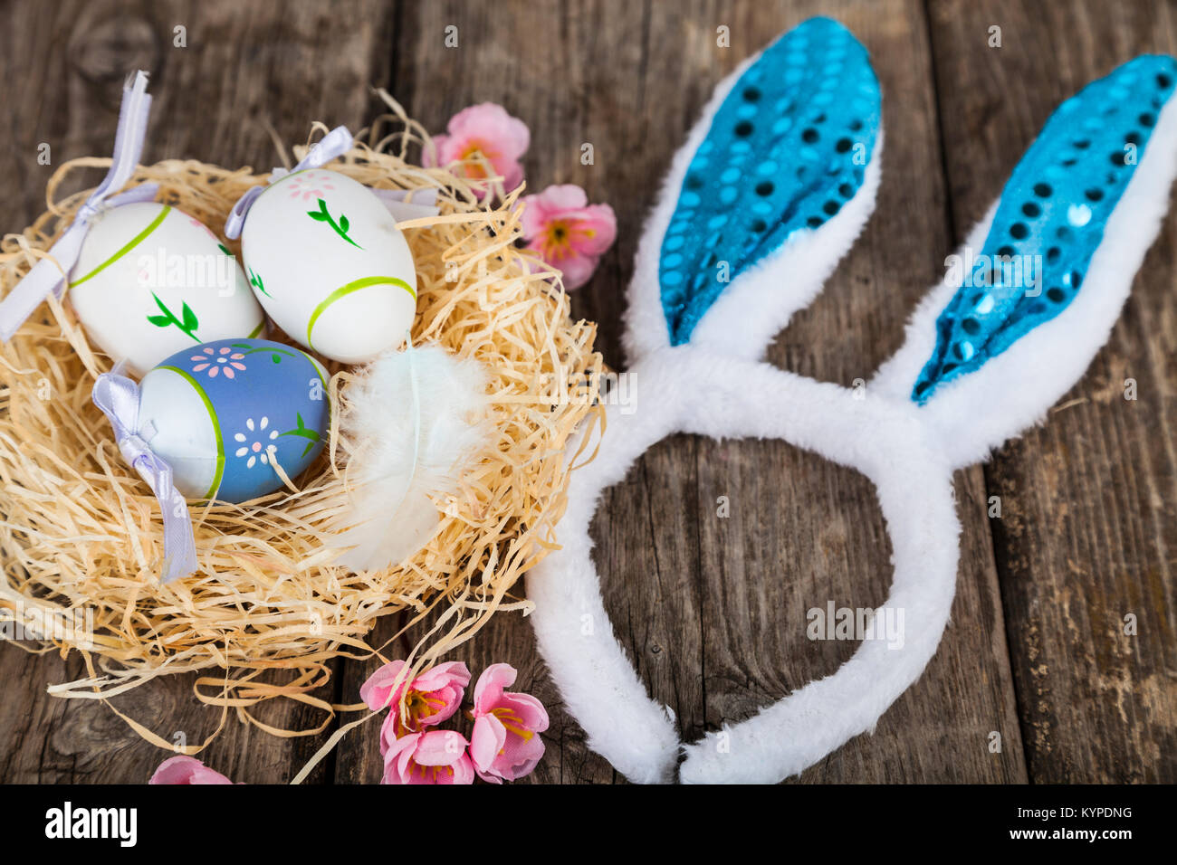 Uova di Pasqua nel nido in legno di colore dello sfondo. La pasqua ancora in vita con orecchie di coniglio, nido, le piume e le uova. Foto Stock