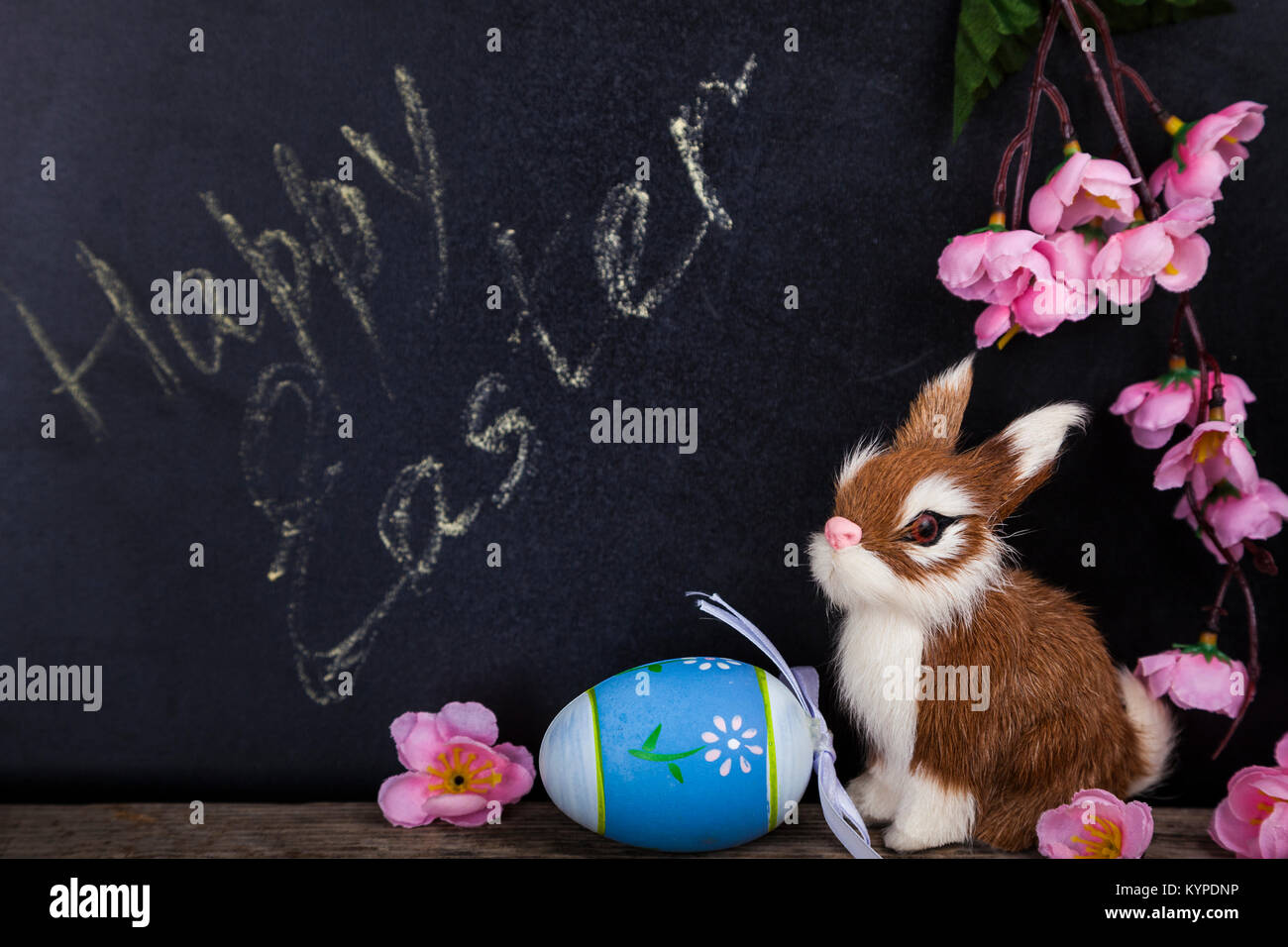 Coniglio giocattolo, fiori e uovo di pasqua su una lavagna sfondo. Pasqua ancora vita.Buona Pasqua. Foto Stock