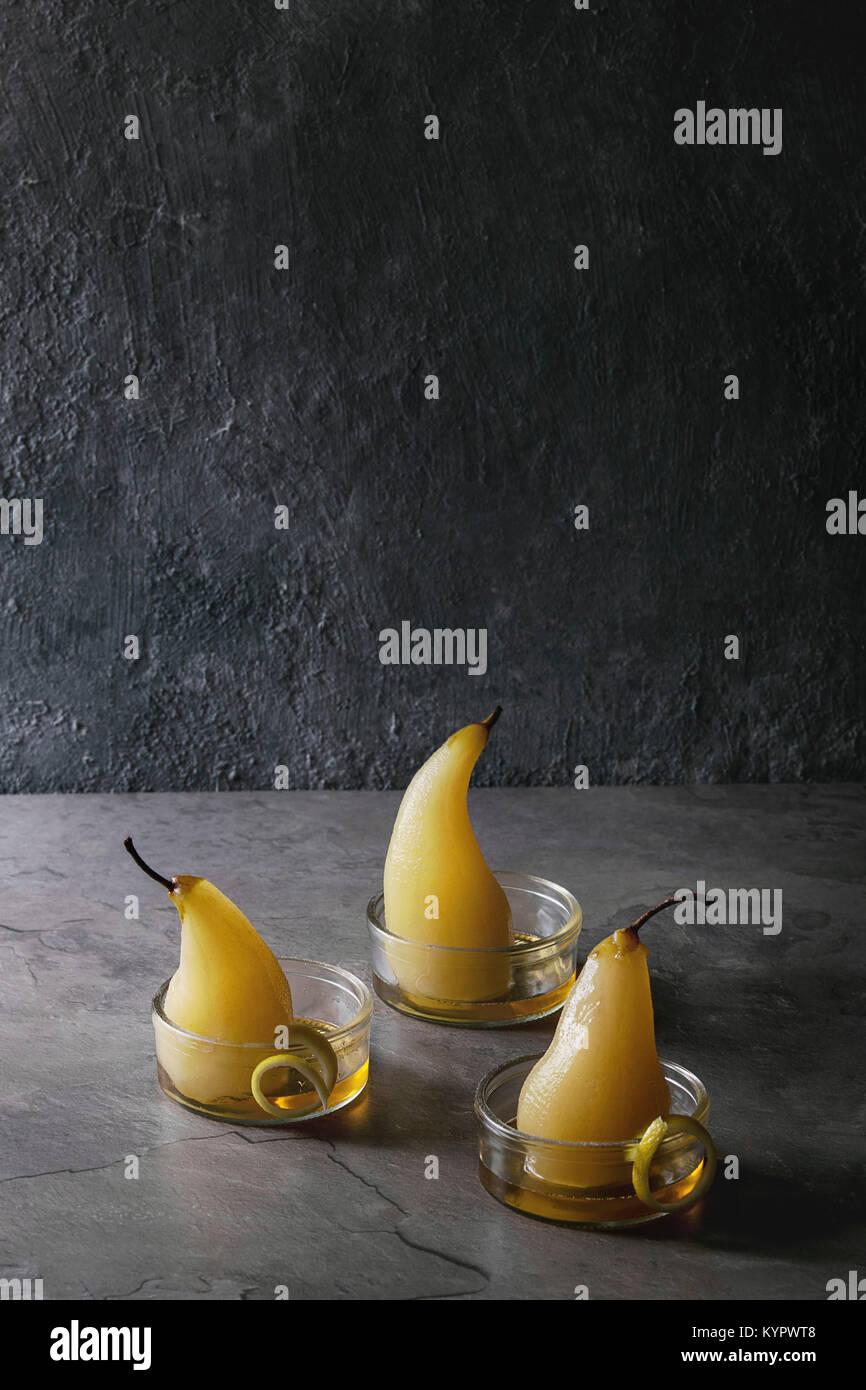 Dolce tradizionale cotto pere al vino bianco servito in ciotole in vetro con sciroppo e la scorza di limone su grigio tabella di texture. Foto Stock