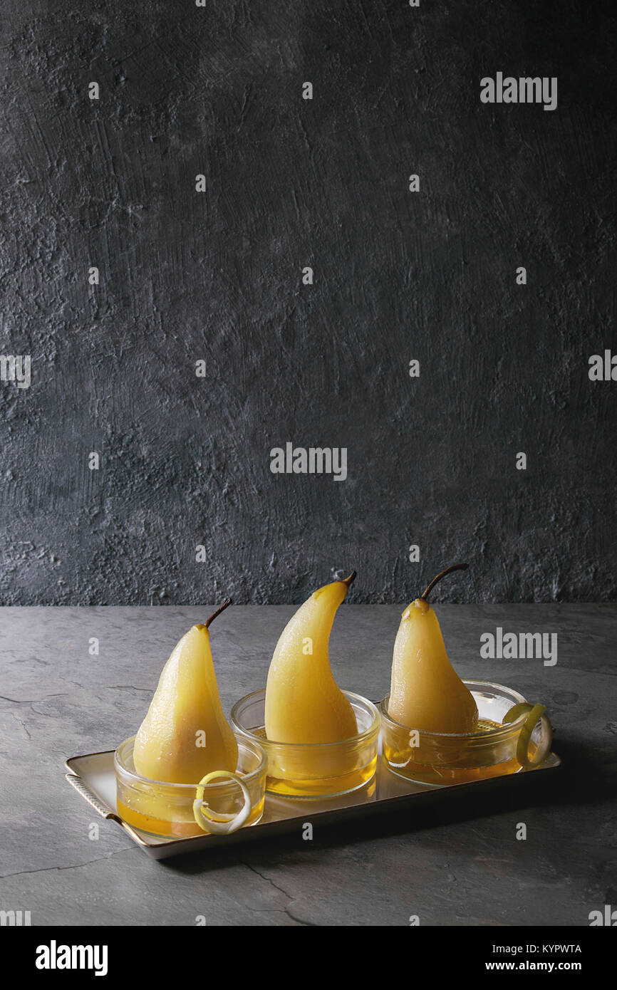 Dolce tradizionale cotto pere al vino bianco servito in ciotole in vetro con sciroppo e la scorza di limone su grigio tabella di texture. Foto Stock