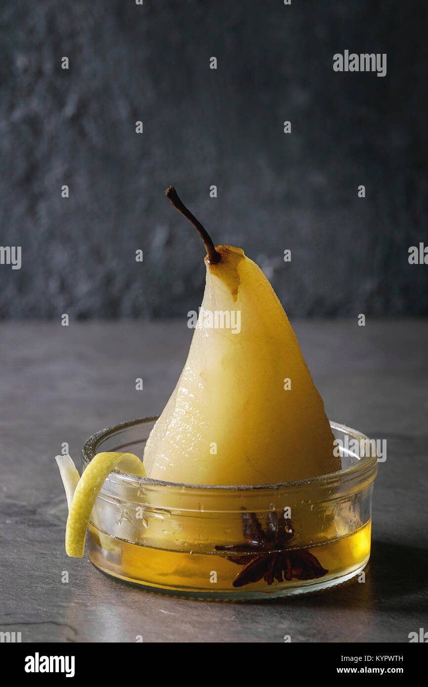 Dolce tradizionale di pera affogata nel vino bianco servito in recipiente di vetro con sciroppo e la scorza di limone su grigio tabella di texture. Foto Stock