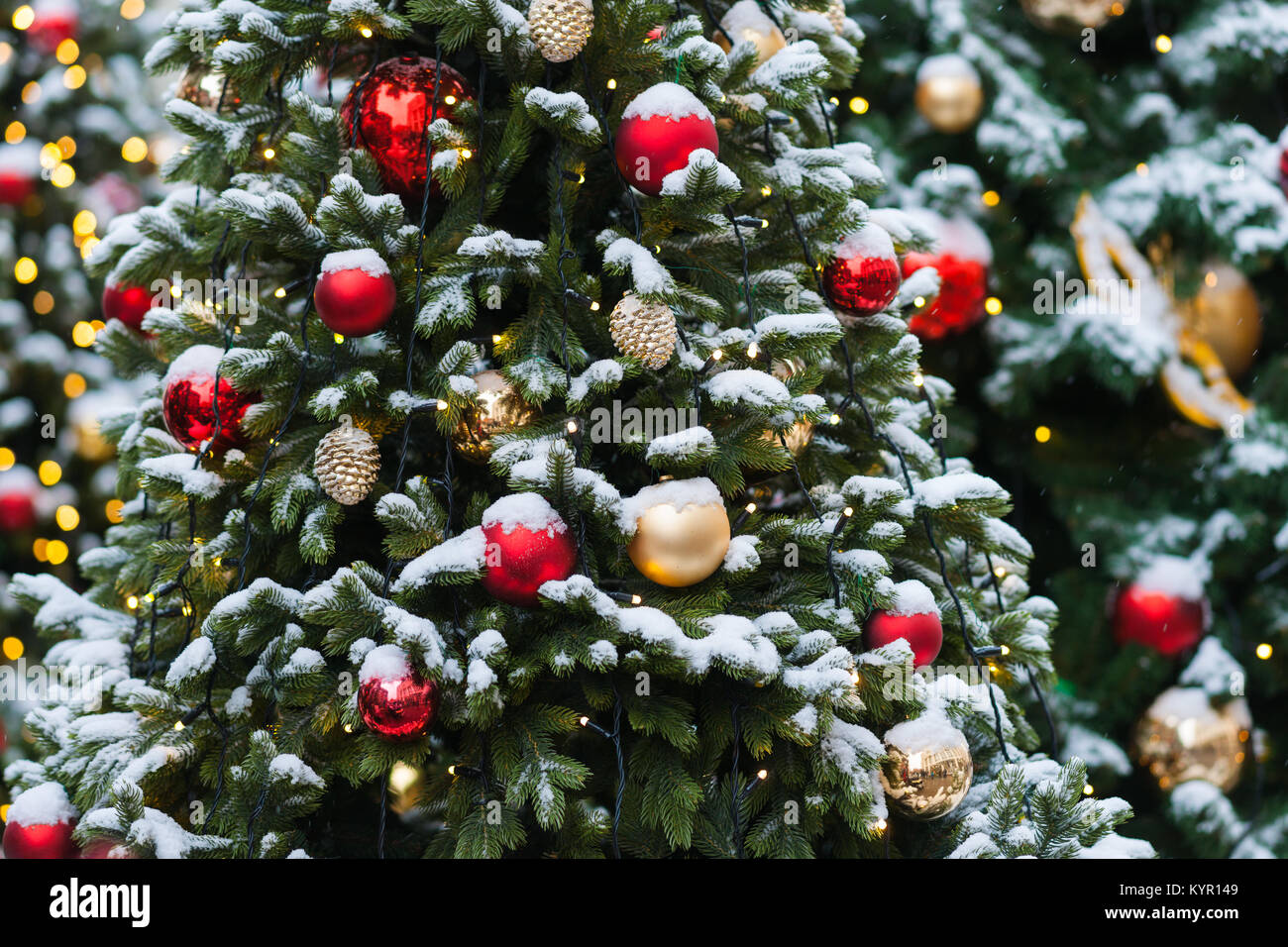 Coperta di neve albero di Natale decorato con il rosso e il giallo di vetro palline di ornamento, giocattoli e luci elettriche. La gioia della stagione di vacanze Foto Stock
