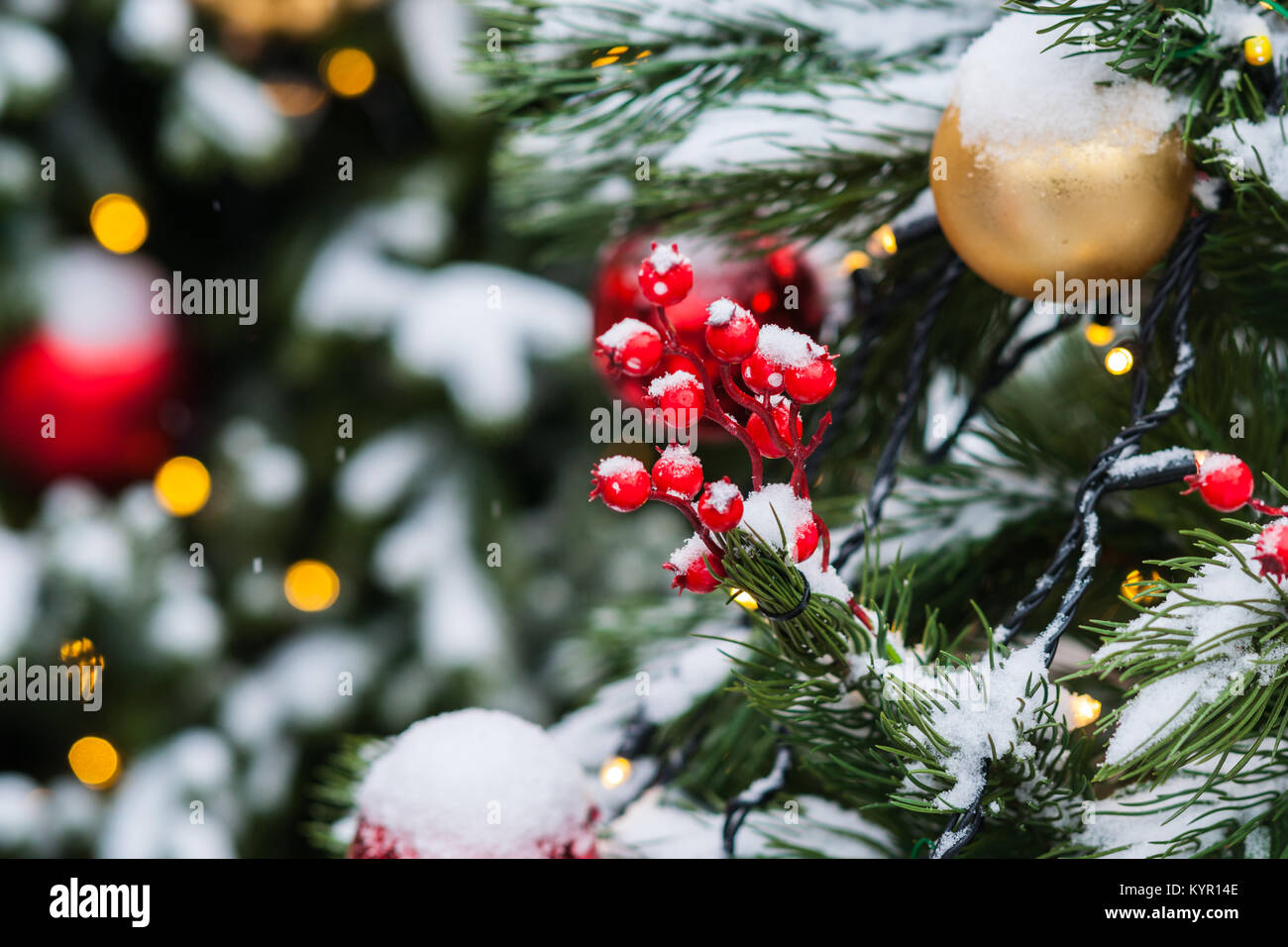 Coperta di neve albero di Natale decorato con il rosso e il giallo di vetro palline di ornamento, giocattoli e luci elettriche. La gioia della stagione di vacanze Foto Stock