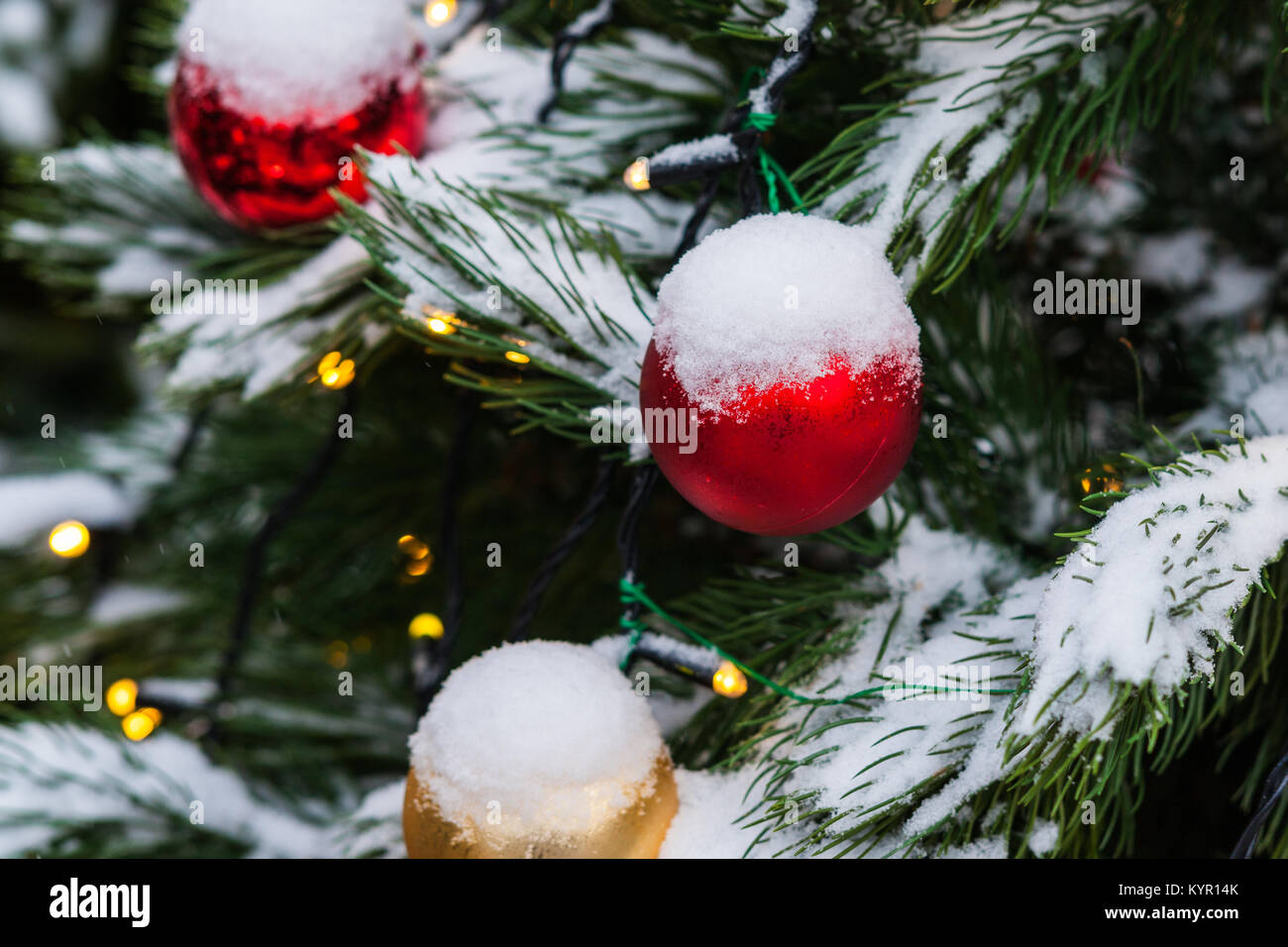 Coperta di neve albero di Natale decorato con il rosso e il giallo di vetro palline di ornamento, giocattoli e luci elettriche. La gioia della stagione di vacanze Foto Stock