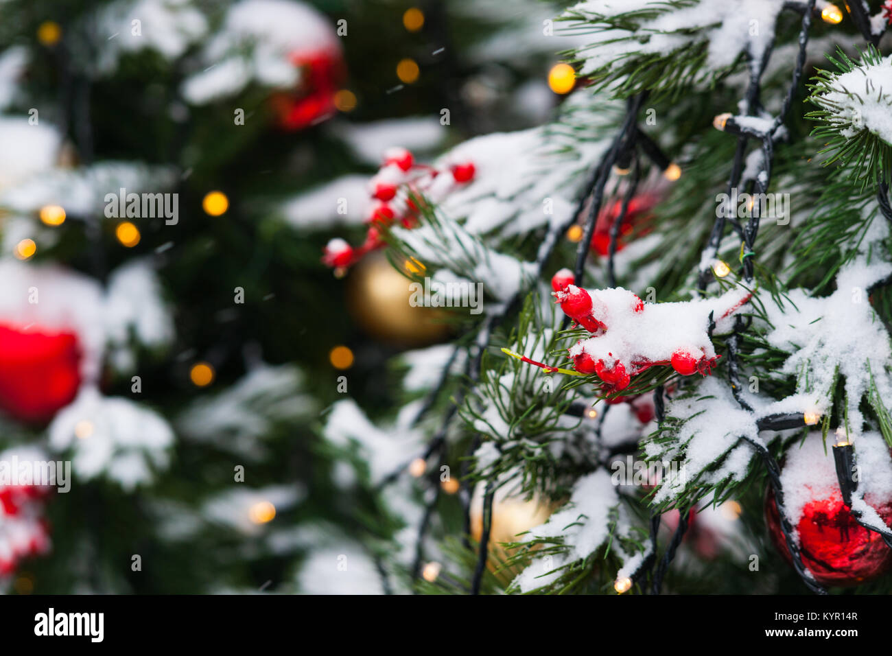 Coperta di neve albero di Natale decorato con il rosso e il giallo di vetro palline di ornamento, giocattoli e luci elettriche. La gioia della stagione di vacanze Foto Stock