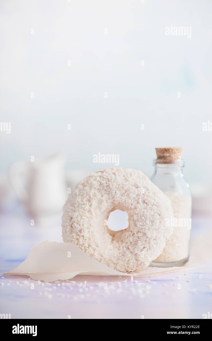 Crema di noce di cocco bianco riempito ciambella con topping di cocco su uno sfondo luminoso. Elevato La chiave fotografia di cibo. Bottiglia di scaglie di cocco Foto Stock