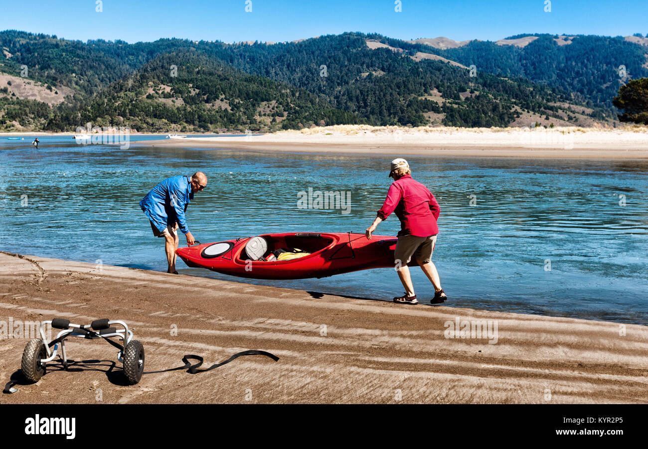 Attivo coppia senior il sollevamento di un kayak nell'acqua. Attività fisica aiuta gli anziani soggiorno montare, sana e indipendente. Posizione: Bolinas, California Foto Stock