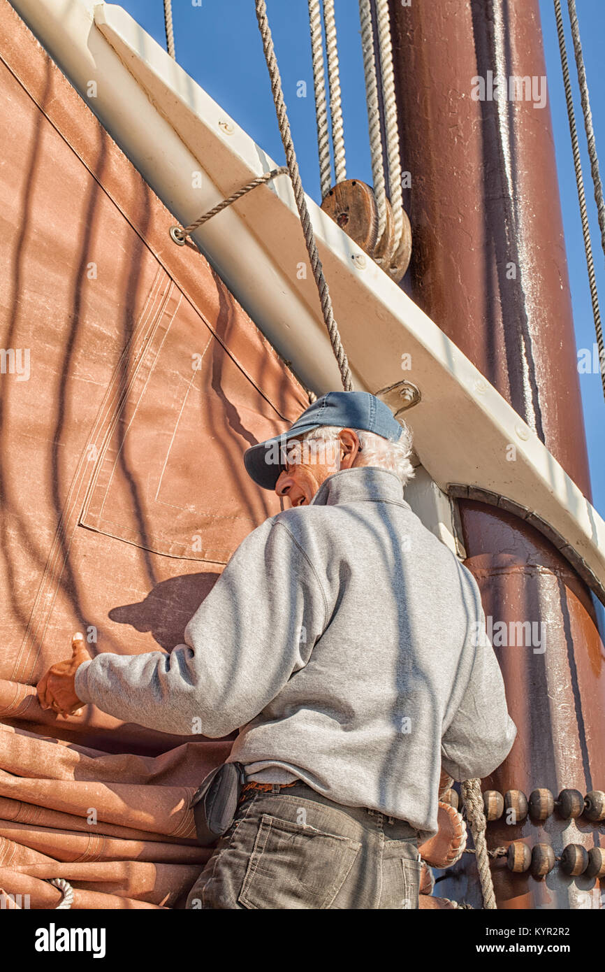 Senior uomo a bordo di una barca a vela aiuta a issare la vela. Viaggi avventura su un tall ship schooner. Concetto per mantenersi in attività di pensionamento. Foto Stock
