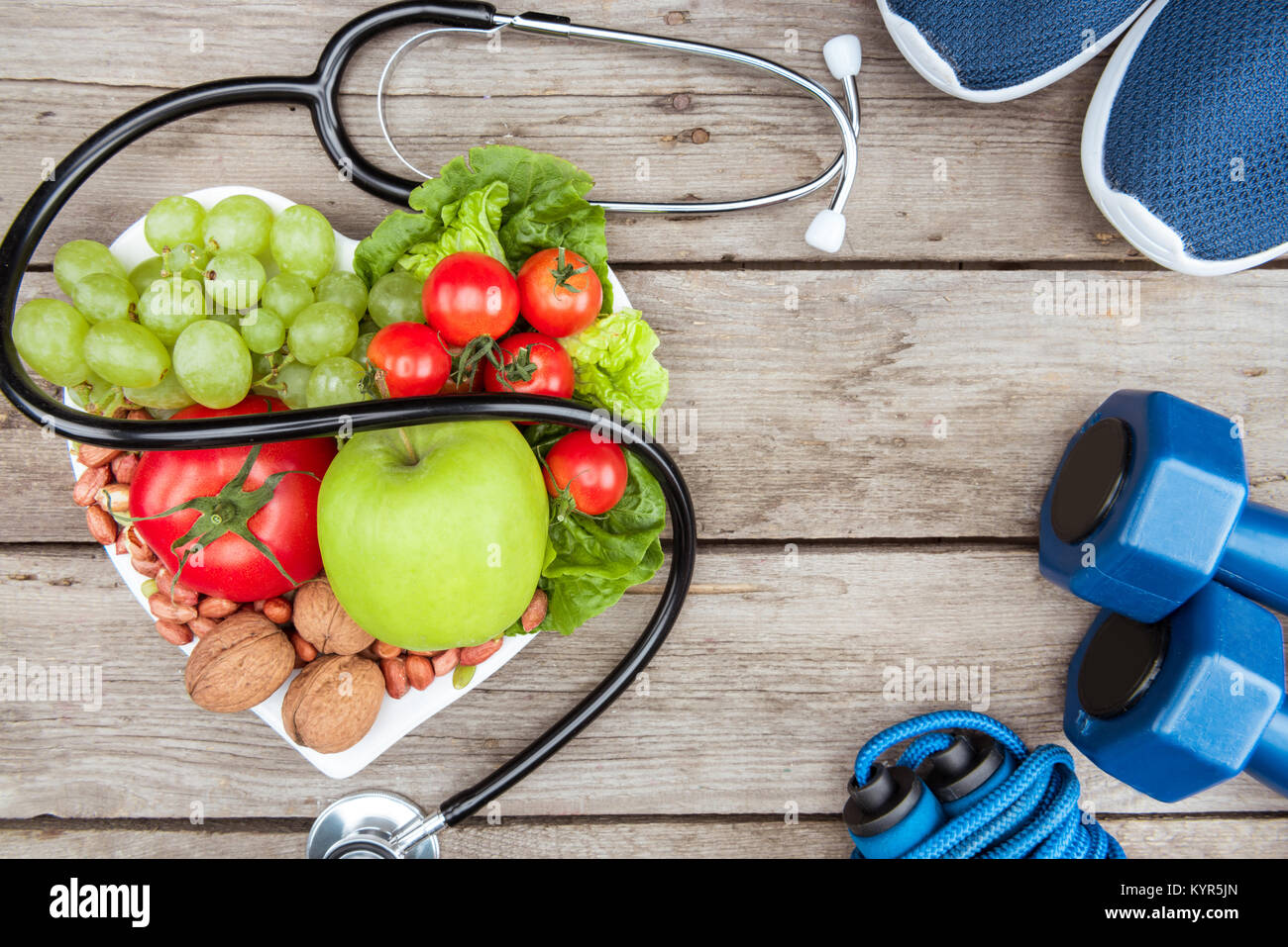 Vista dall'alto di uno stetoscopio, ortaggi e frutta e attrezzature sportive su una superficie di legno, uno stile di vita sano concetto Foto Stock