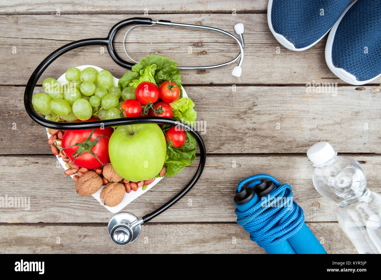 Vista dall'alto di uno stetoscopio, ortaggi e frutta e attrezzature sportive su una superficie di legno, uno stile di vita sano concetto Foto Stock