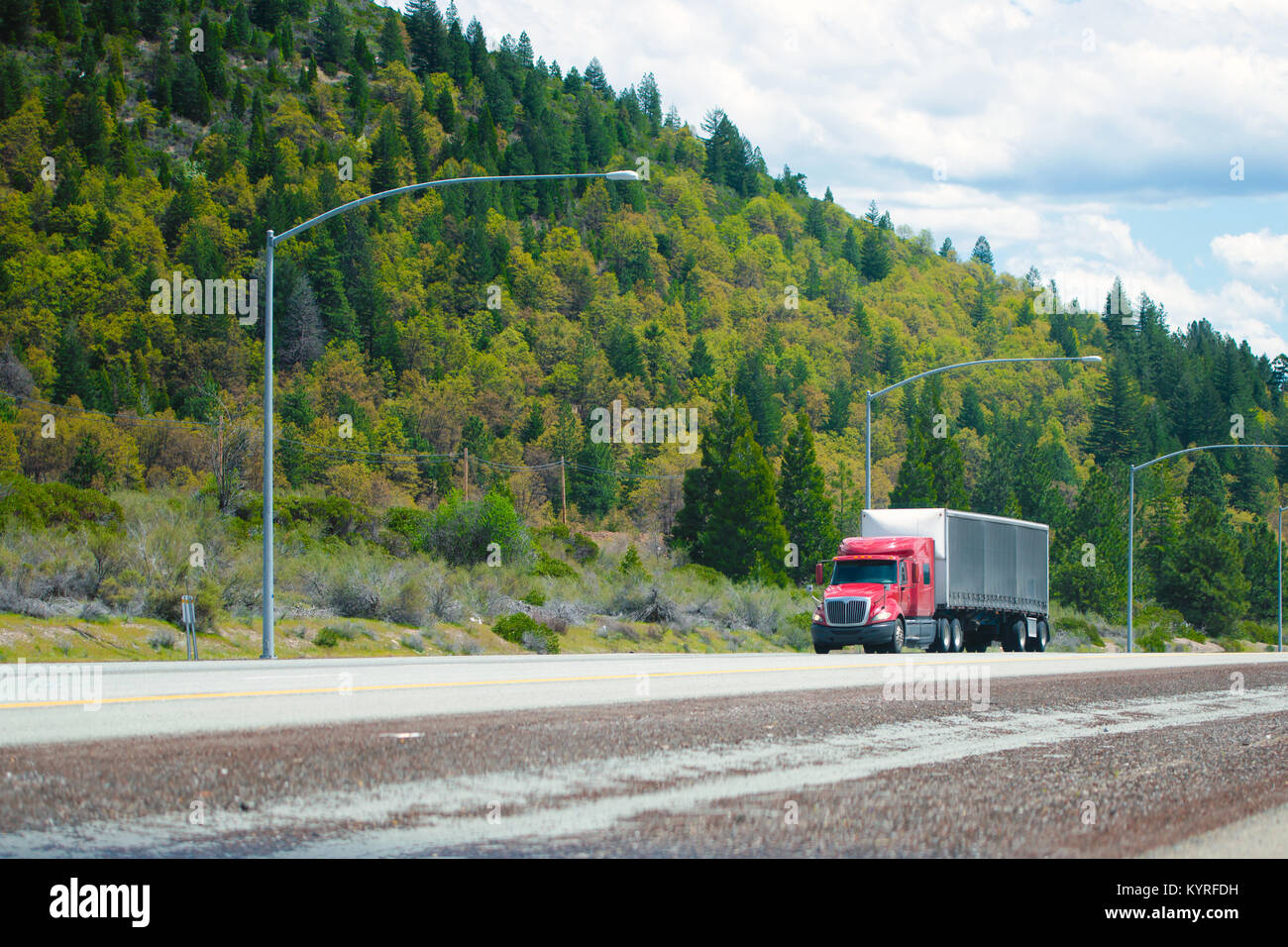 Red big rig lucido moderno semi-carrello con nero tarp dry van rimorchio con spoiler aerodinamico nella parte anteriore del rimorchio si muovono sul rettilineo diviso interstate Foto Stock