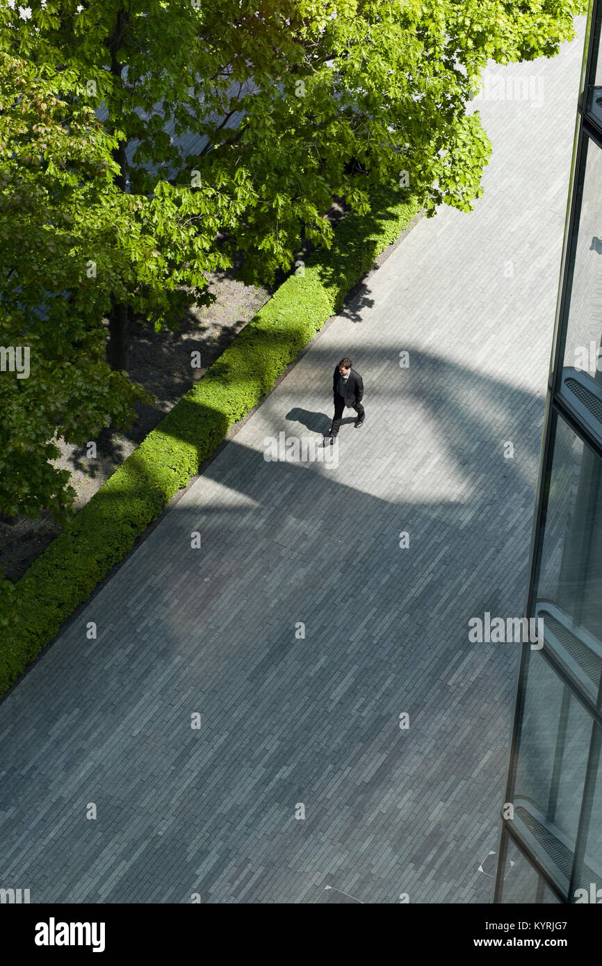 Guardando verso il basso su un lavoratore della città passeggiando lungo il cammino o marciapiede accanto a bright green alberi nel quartiere finanziario Foto Stock