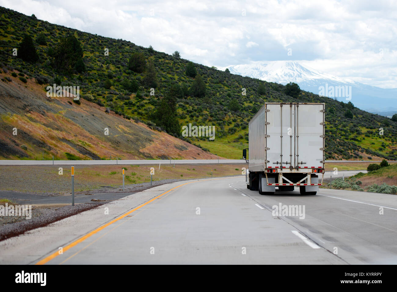 Un big rig semi carrello con un dry van rimorchio per long haul freight girare sul dividendo di avvolgimento autostrada con verdi alberi sulle colline stradale Foto Stock