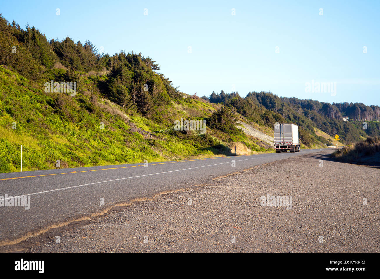 Classic semi carrello con un dry van rimorchio lascia nella distanza oltre la linea di orizzonte su una strada solitaria con erba verde lungo l'oceano pacifico Foto Stock
