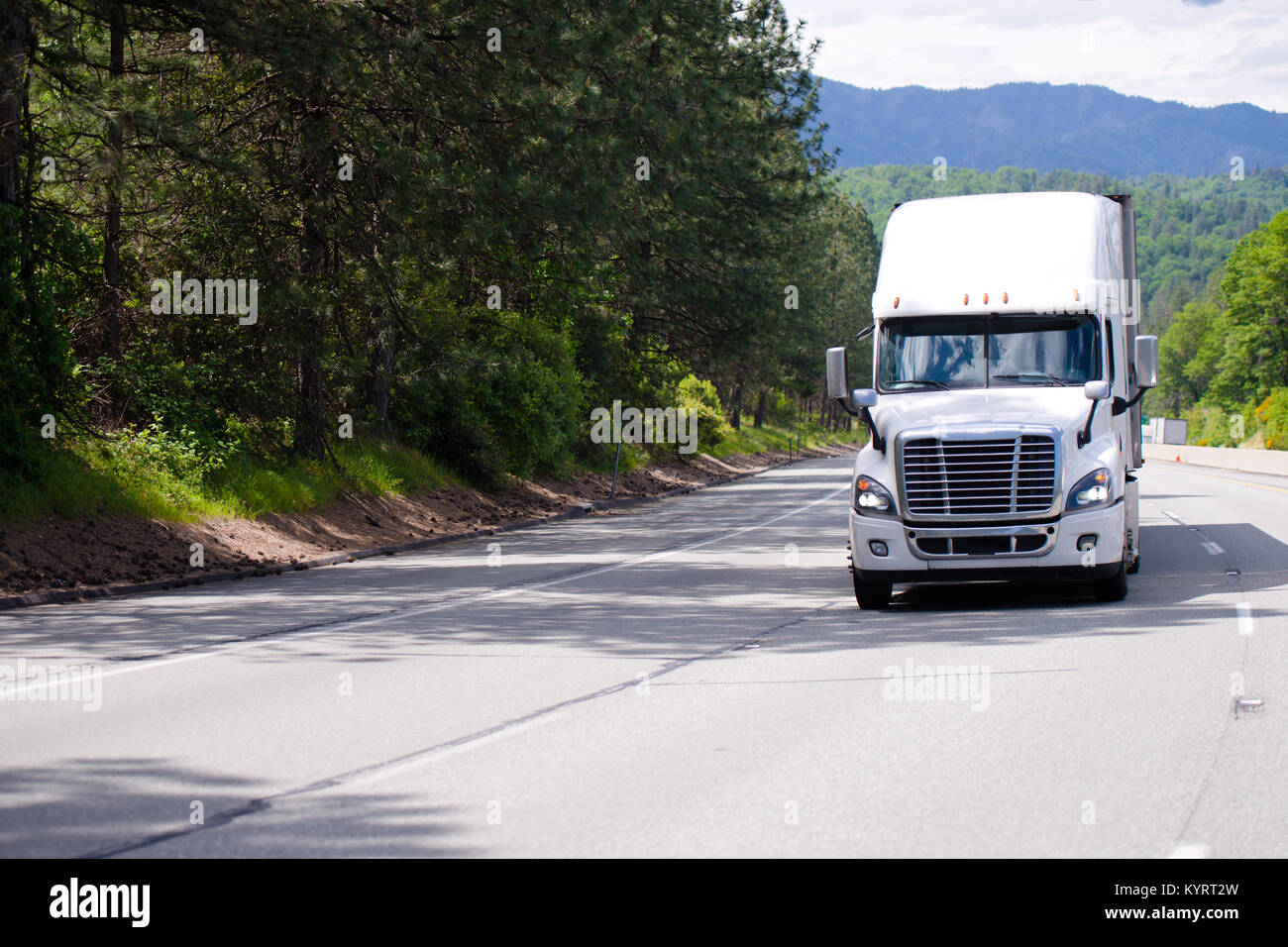 Bianco moderno big rig semi carrello con griglia cromata e dry van rimorchio il pilotaggio tramite ampia multi-linea autostrada con alberi verdi e ombra Foto Stock