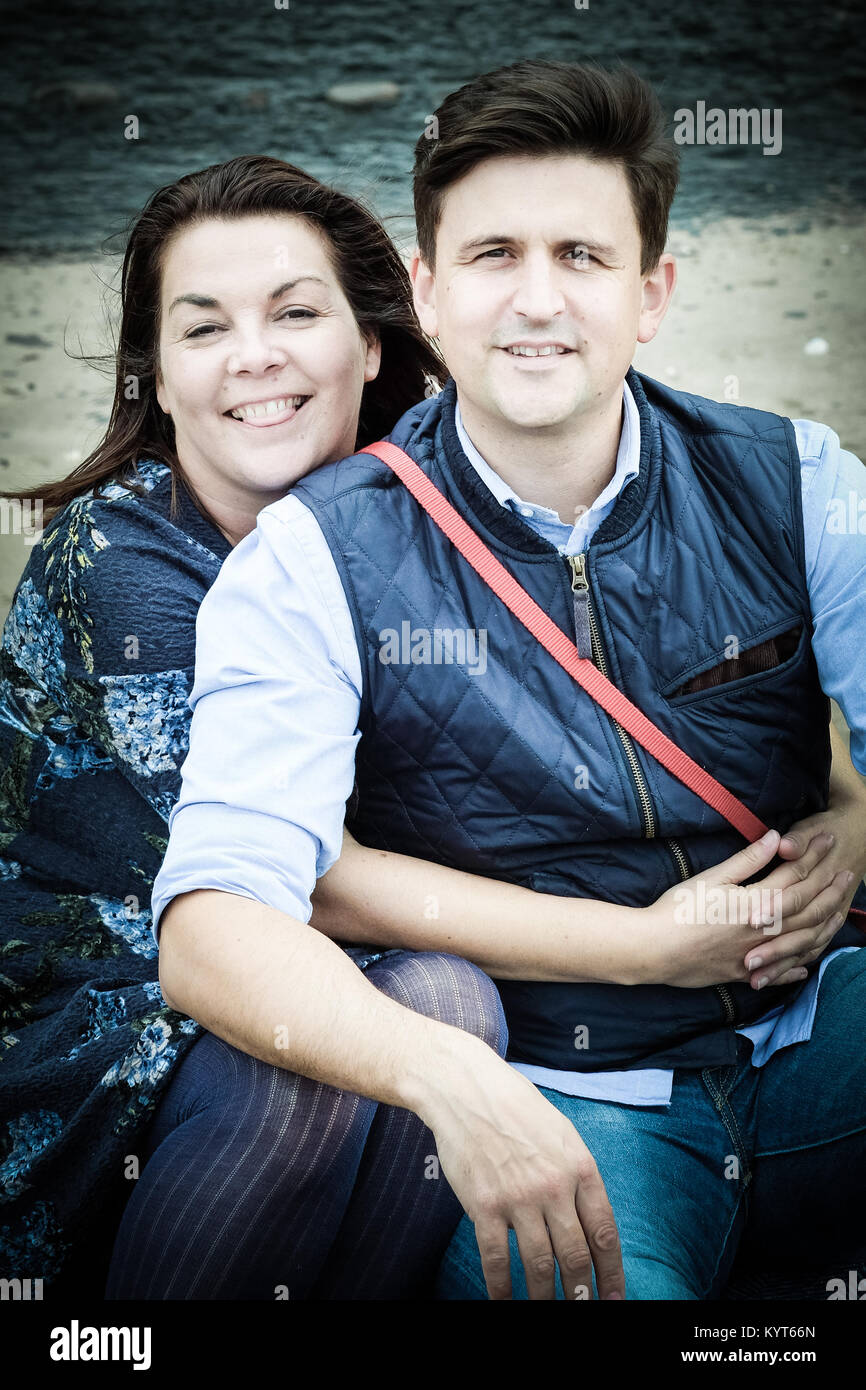 Marito e moglie, genitori, giovane, avvolgente, rivolta verso la telecamera in Runswick Bay, Yorkshire, Regno Unito Foto Stock