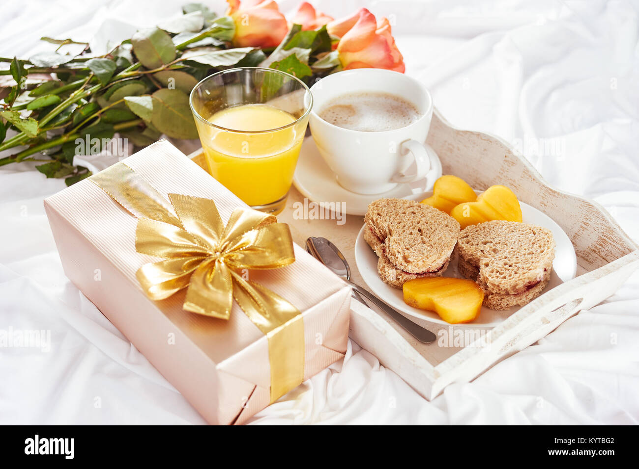 La prima colazione, orange rose e presente con grande golden bow-nodo sul lenzuolo bianco per il giorno di San Valentino Foto Stock