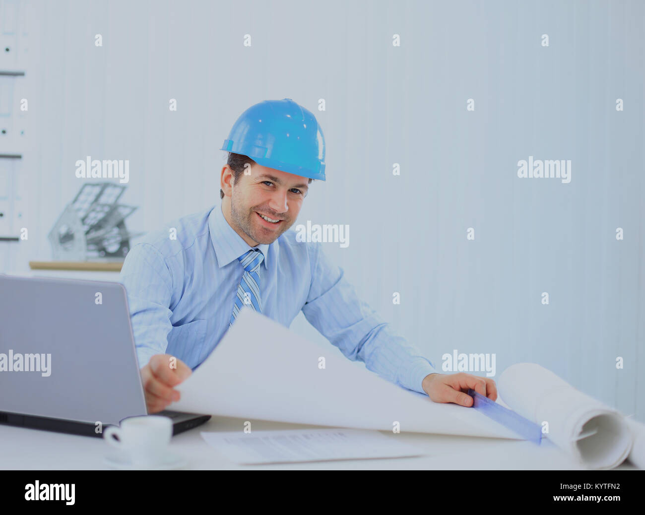 Architetto cerca lavoro in ufficio alla scrivania. Indossare casco e prendere appunti su carta. Foto Stock