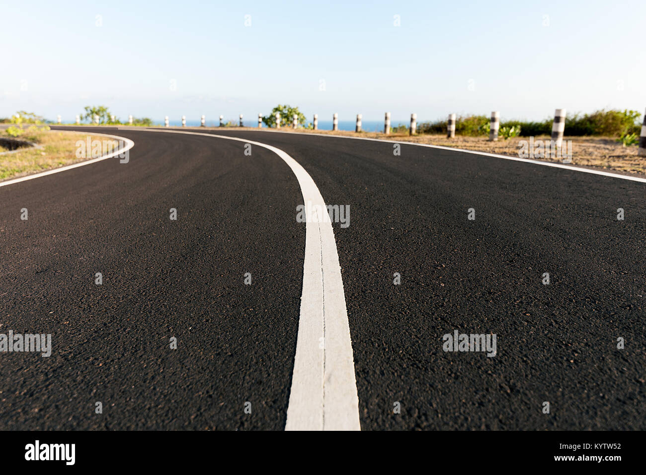 La Tarmac strada costiera intorno a bordo scogliera curva, con il mare blu back drop. Foto Stock