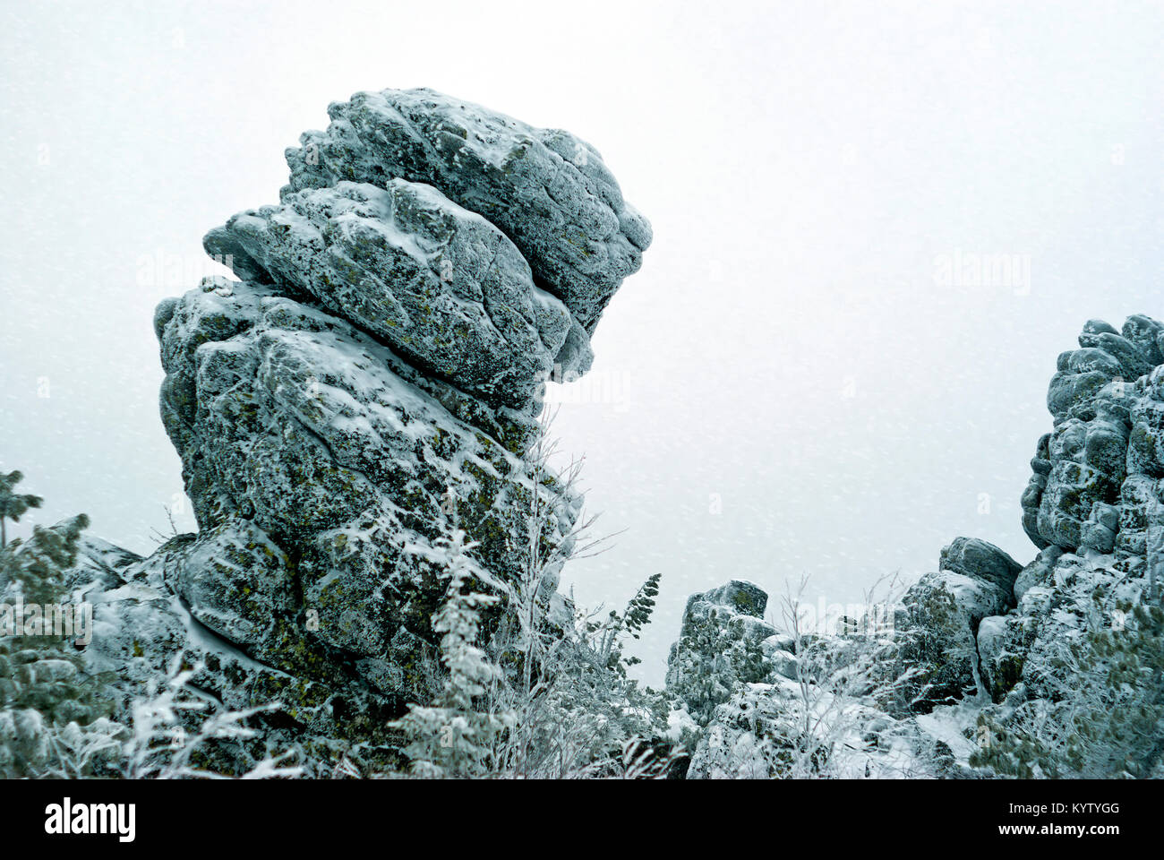 Un enorme inclinato incrinato icy rock oltre la foresta subartiche contro un bianco cielo nevoso Foto Stock