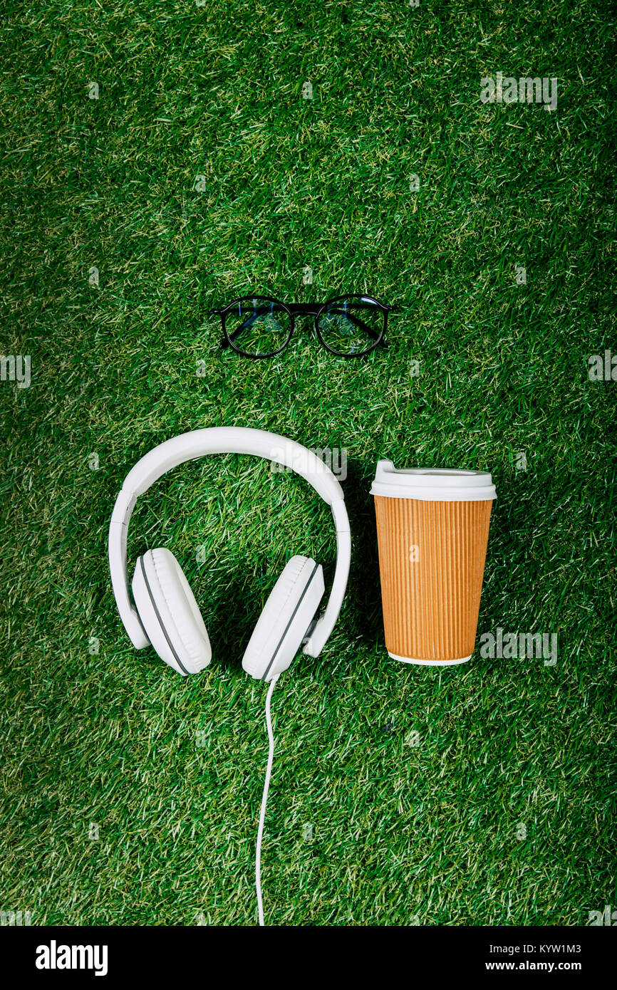 Vista dall'alto di cuffie, occhiali e caffè di andare sul prato verde Foto Stock