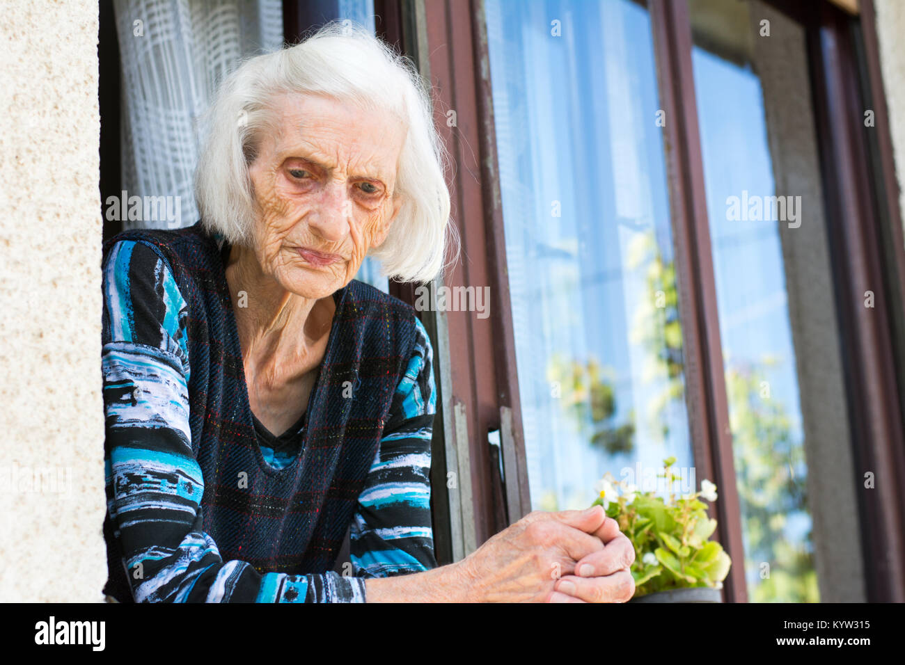 Malinconici nonna nel suo 90s in corrispondenza della finestra di casa da solo Foto Stock