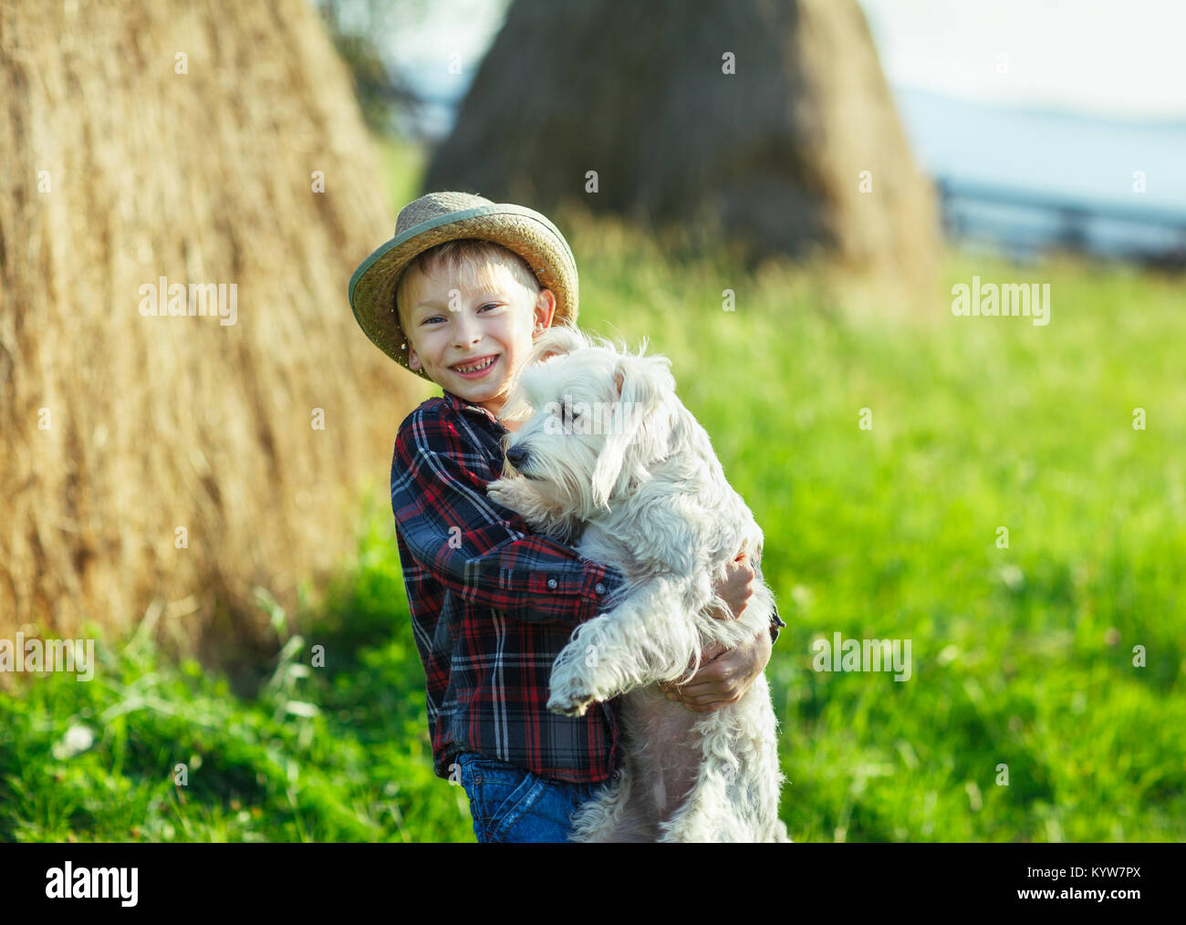 Ragazzo abbraccia in piedi con il cane, half-size ritratto all'aperto, pagliaio sfondo. Giovane uomo animale e gioire nel verde della campagna. Forte amici Foto Stock