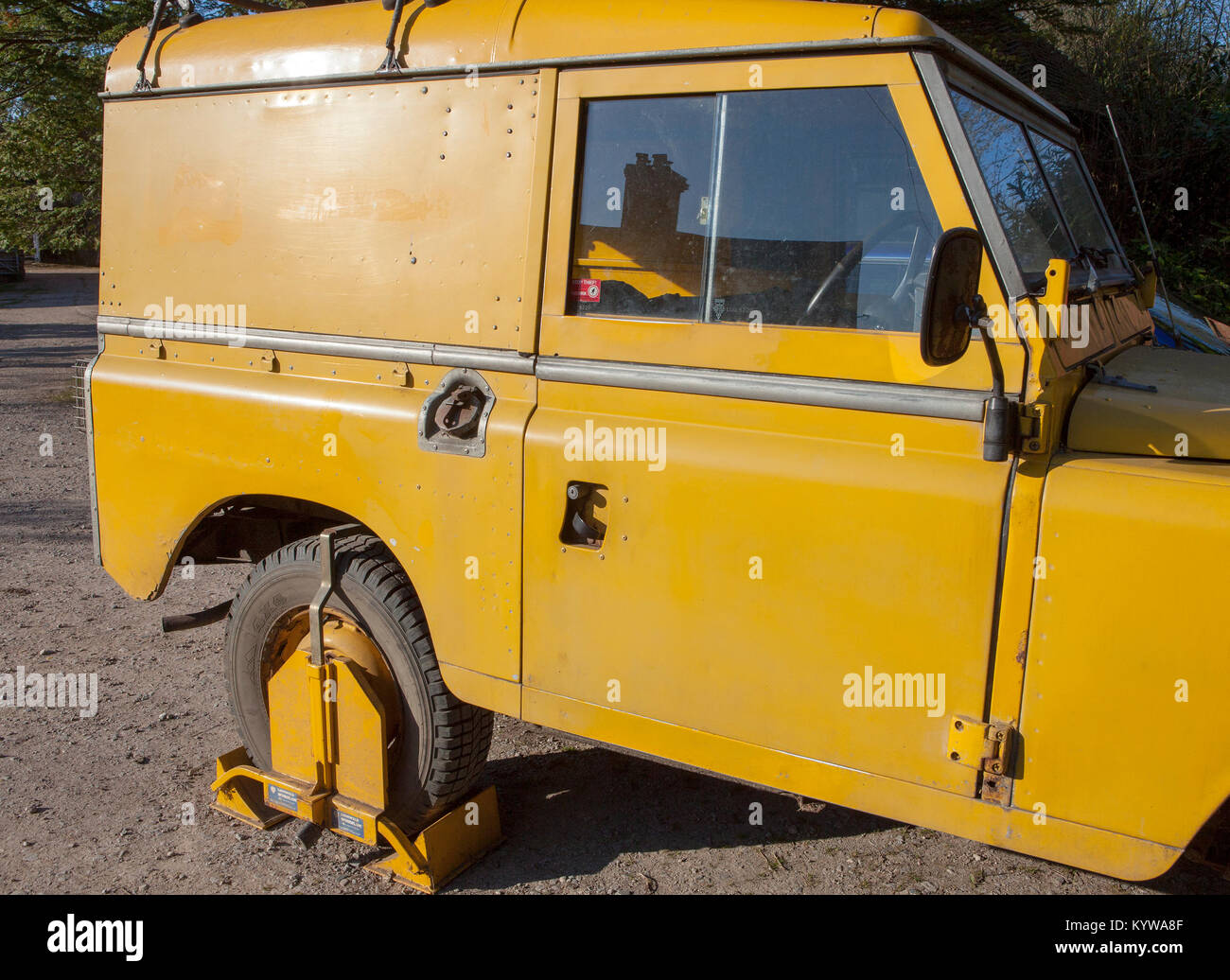 Un giallo a morsetto di bloccaggio di ruota su un giallo Land Rover Serie 3. Parcheggiato su un terreno privato, il morsetto è a dissuadere i ladri. Foto Stock