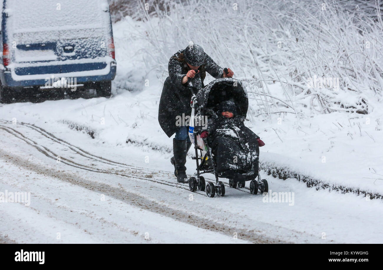 Eaglesham, Glasgow. 16 gennaio, 2018. Spingendo una carrozzina non è facile dopo una nevicata rende le strade e marciapiedi scivolosi e pericolosi come questo giovane madre e il suo bambino scoprire sulla loro strada di casa. Credito: Findlay/Alamy Live News Foto Stock