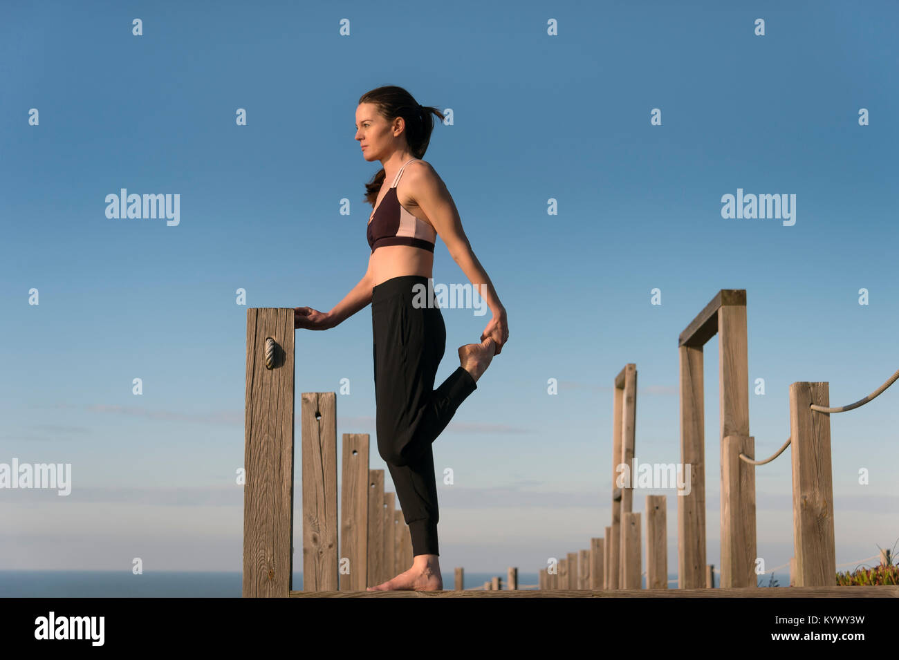 Donna facendo una gamba tratto al di fuori di indossare un reggiseno sportivo e gambali Foto Stock