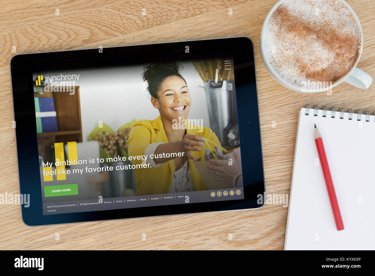 La sincronia sito finanziario su un tablet iPad, su di un tavolo di legno accanto a un blocco note, matita e tazza di caffè (editoriale solo) Foto Stock