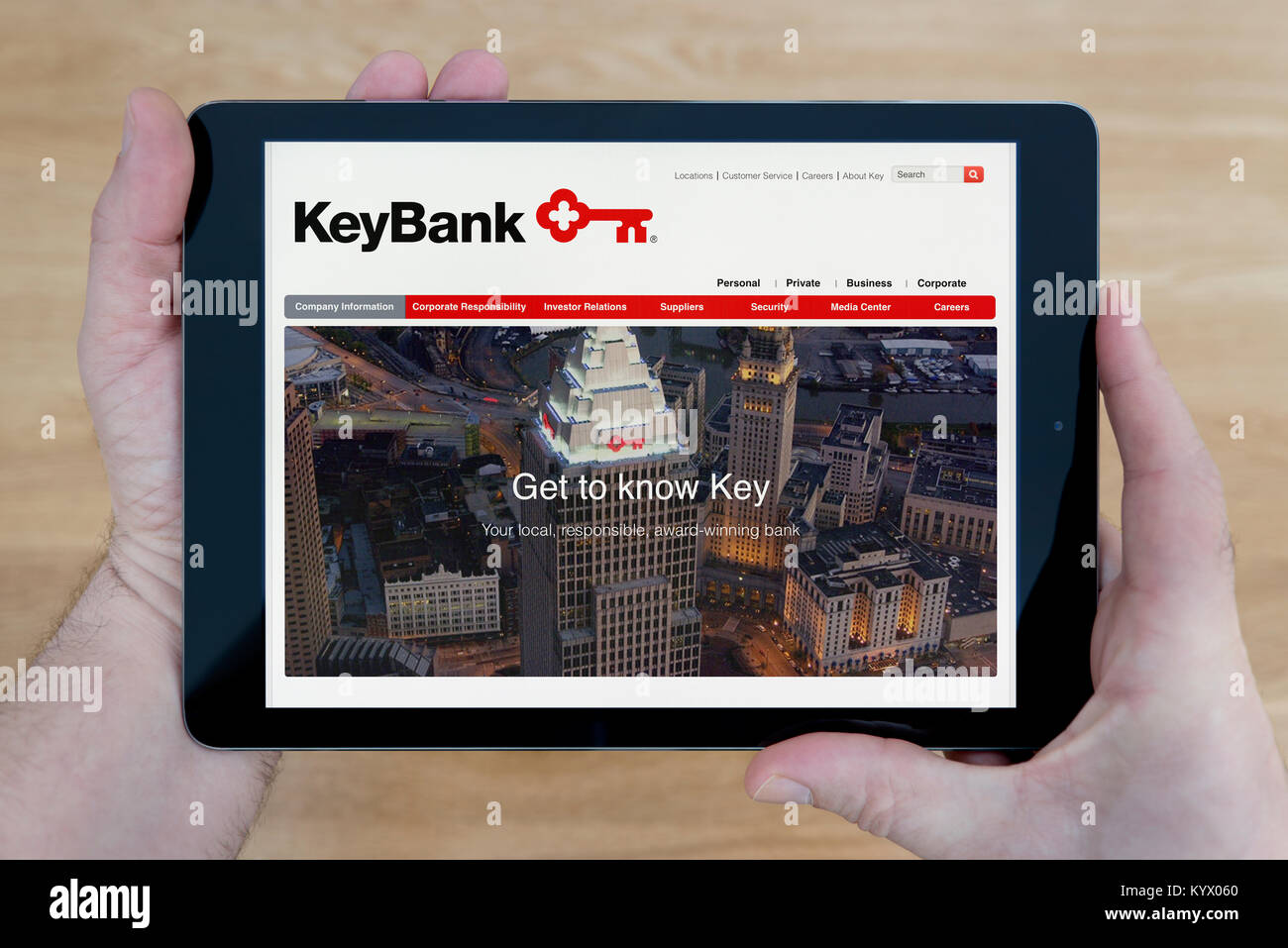 Un uomo guarda il sito KeyBank sul suo iPad dispositivo tablet pc, con un tavolo di legno top sfondo (solo uso editoriale) Foto Stock