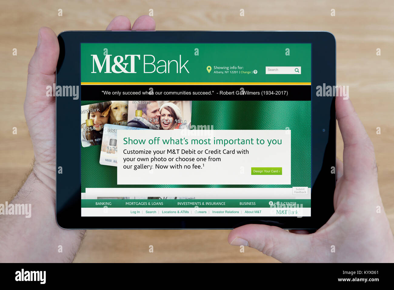 Un uomo guarda al M&T Bank sito sul suo iPad dispositivo tablet pc, con un tavolo di legno top sfondo (solo uso editoriale) Foto Stock