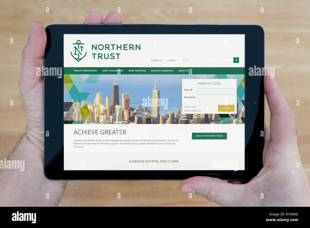 Un uomo guarda il Northern Trust sito sul suo iPad dispositivo tablet pc, con un tavolo di legno top sfondo (solo uso editoriale) Foto Stock