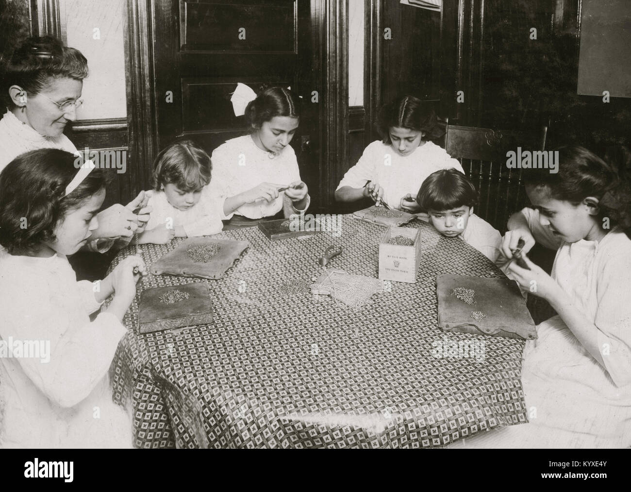 Donna e bambini intorno ad un tavolo per rendere le catene per le borsette Foto Stock