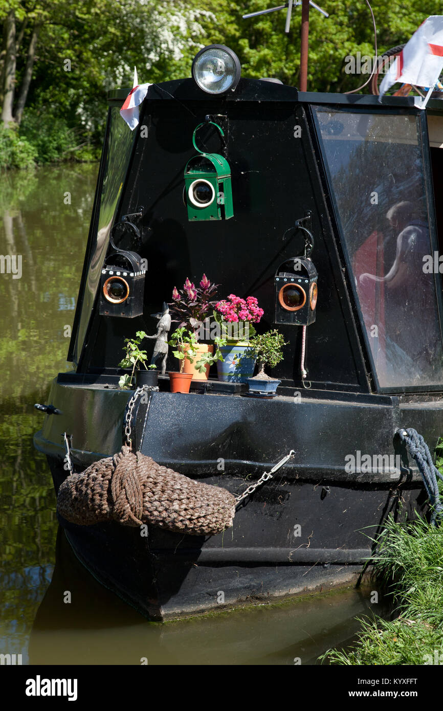 Narrowboat nero sul Grand Union Canal decorate con la vecchia strada pericolo lampade e vasi di piante. Foto Stock