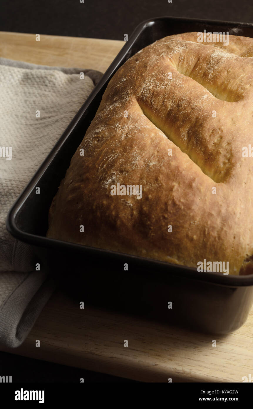 Pane appena sfornato fatta in casa della pagnotta di pane organico dello stagno sul tagliere di legno con ripiegato presina a lato. Foto Stock