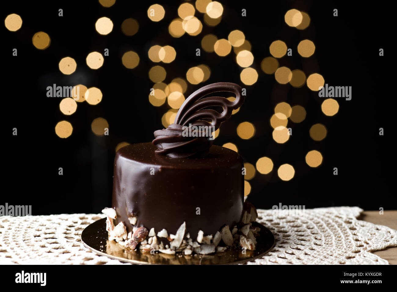 Orizzontale basso studio chiave accesa ganache al cioccolato torte con bordo di mandorle tritate e delicate decorazioni scolpite sulla parte superiore. Bokeh luci soft focus. Foto Stock
