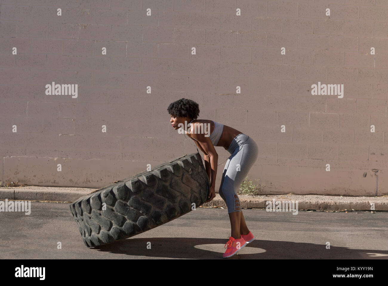 Donna di sollevamento carrello pneumatico mentre si esercita contro la parete Foto Stock