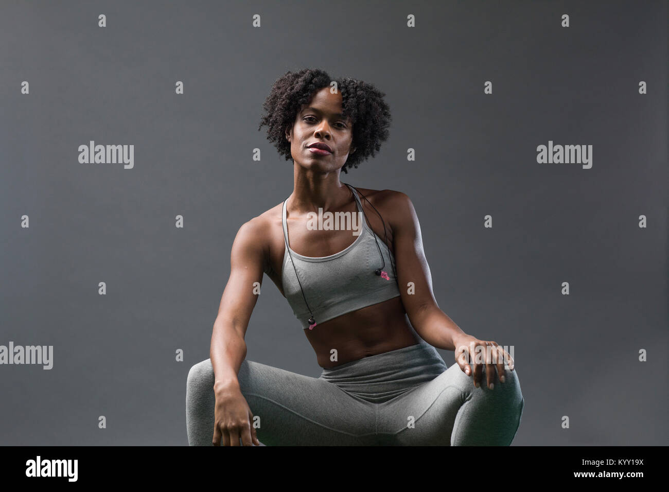 Ritratto di donna fiducioso di indossare abbigliamento sportivo mentre è seduto contro la parete in palestra Foto Stock