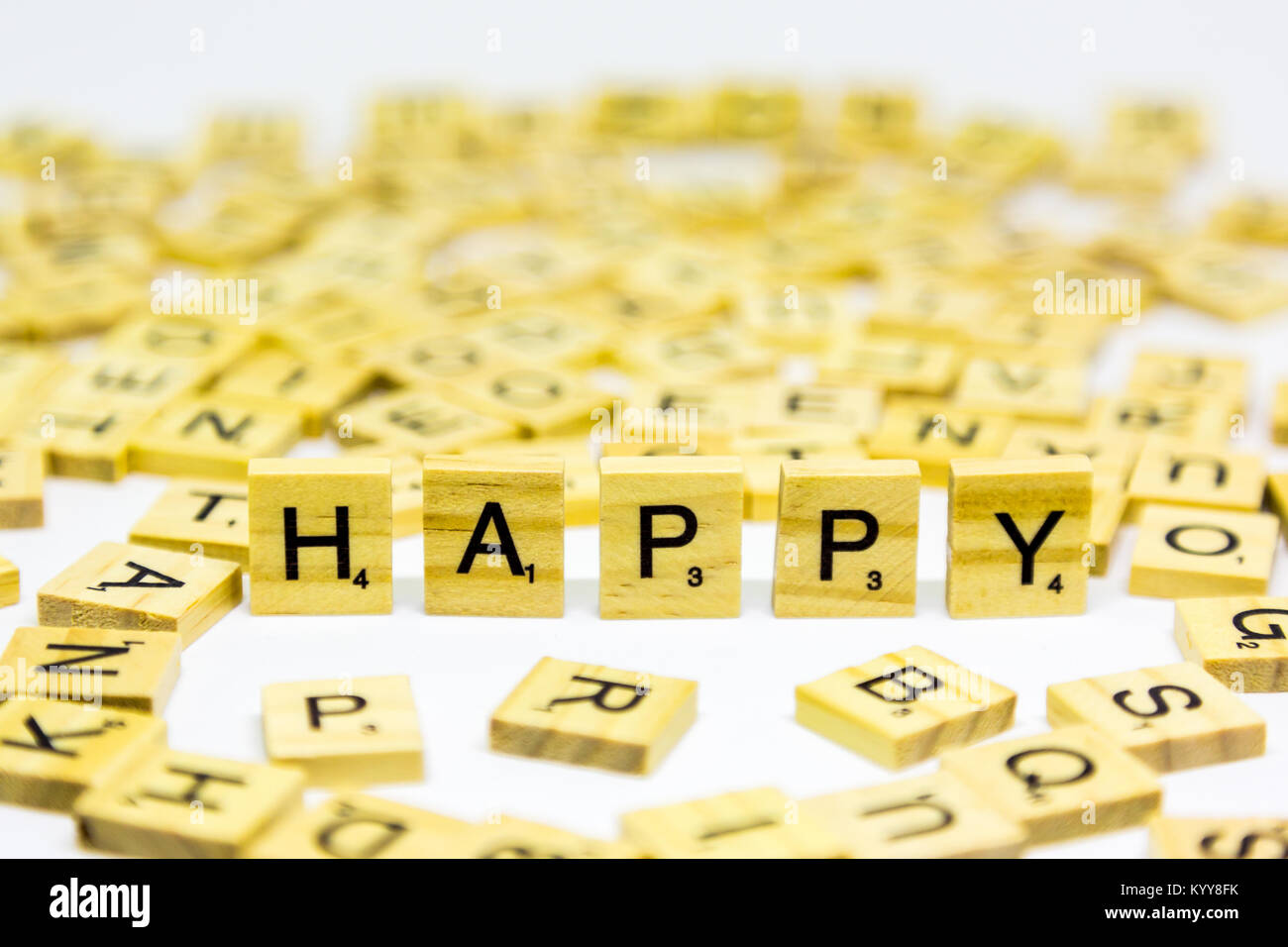 La parola felice in piedi realizzato da legno lettere di scrabble su sfondo bianco Foto Stock